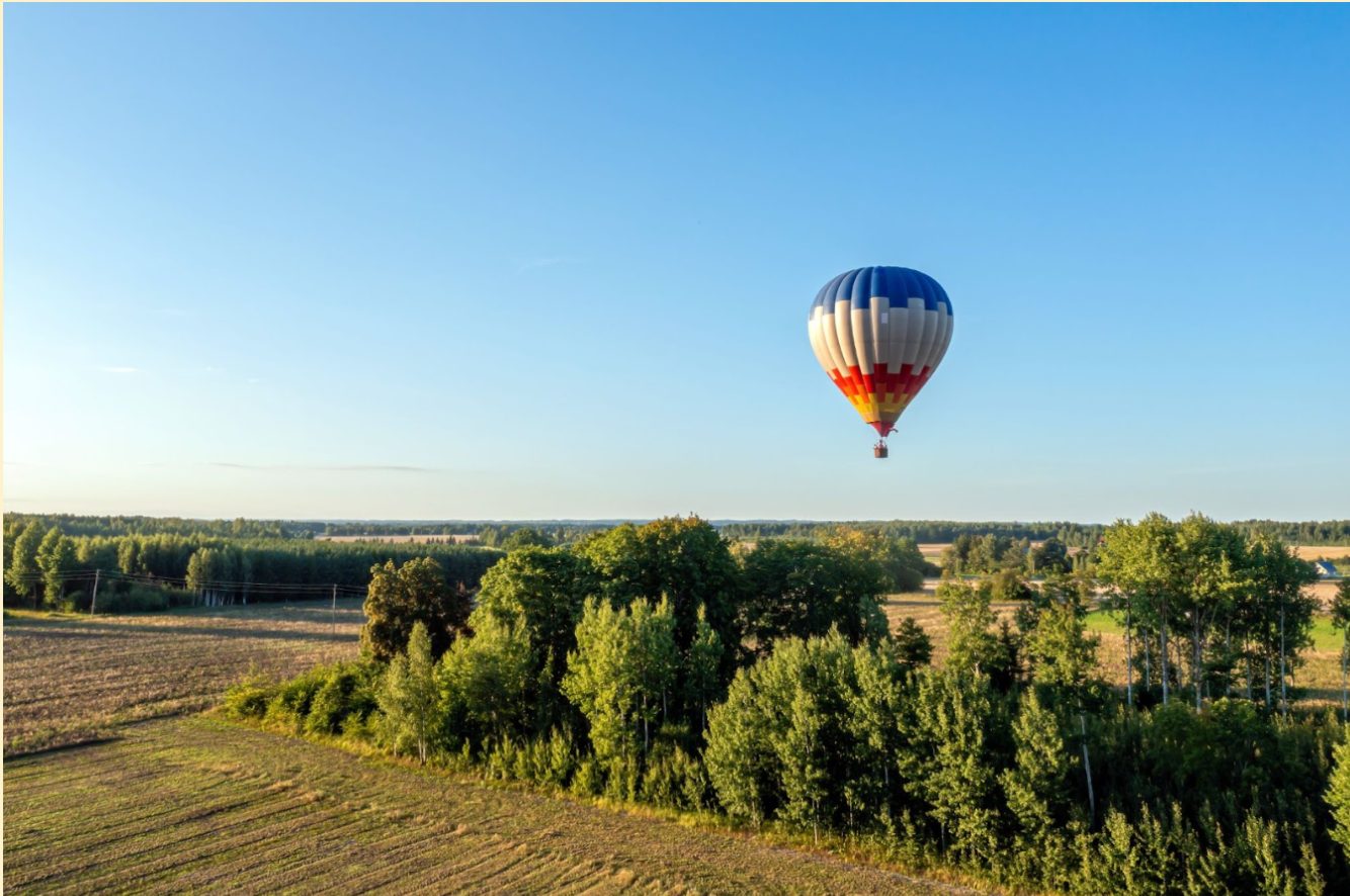 Luchtballon zweeft boven velden en bomen bij helder weer.