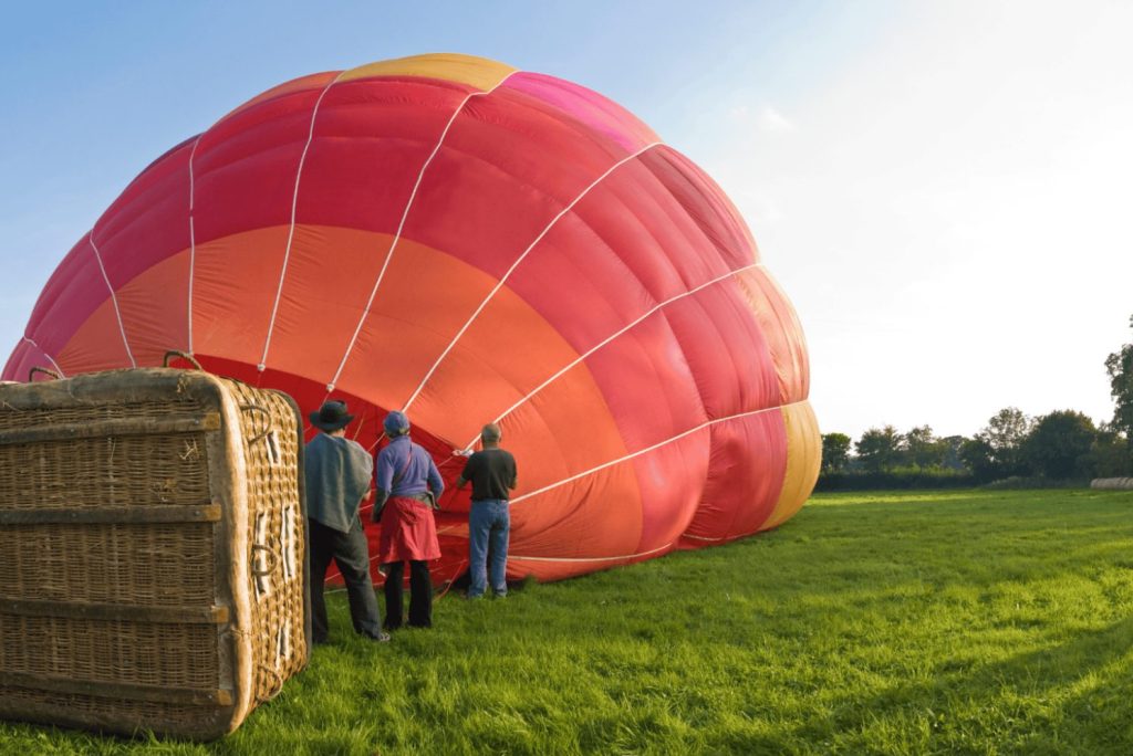 Crew helpt bij het klaarmaken van een rode luchtballon op een veld.