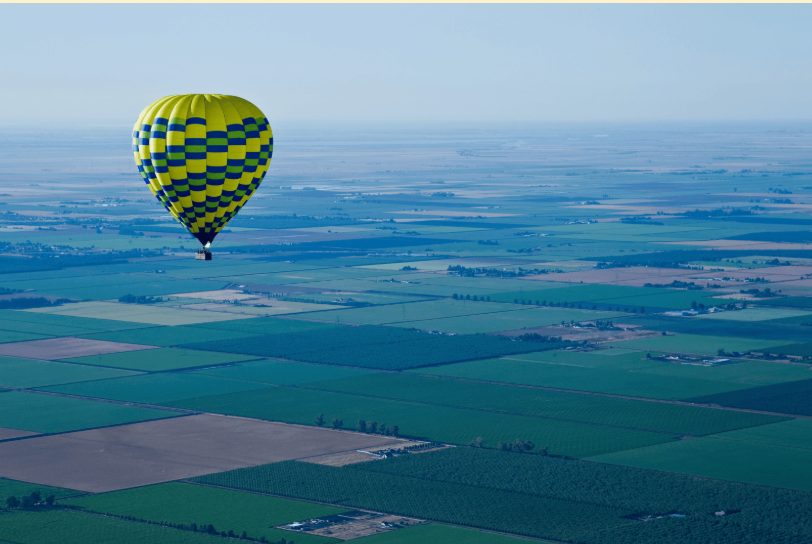 Luchtballon zweeft op grote hoogte boven uitgestrekt landschap.