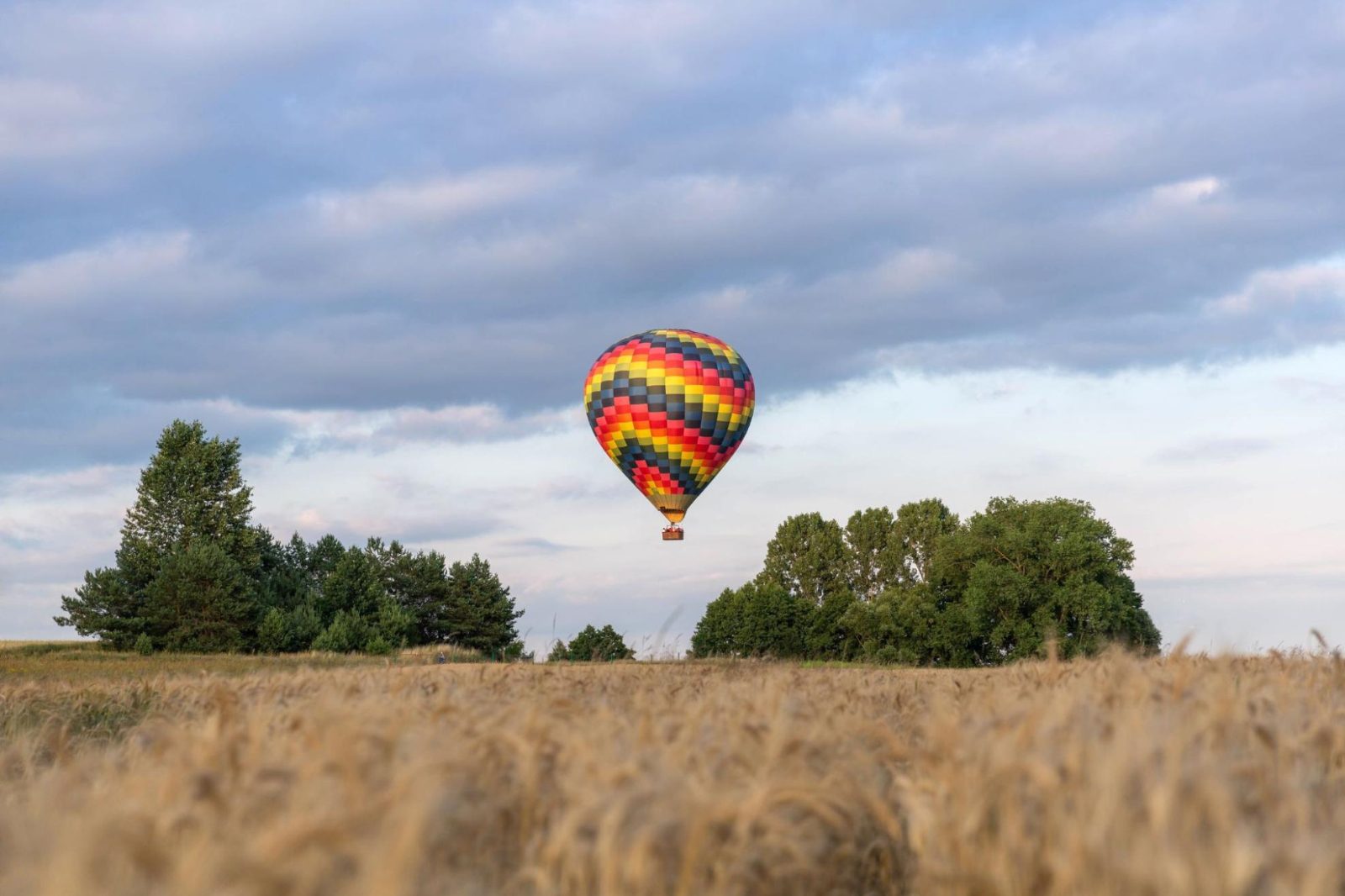 Kleurrijke luchtballon zweeft laag boven een veld in Deinze bij zonsondergang