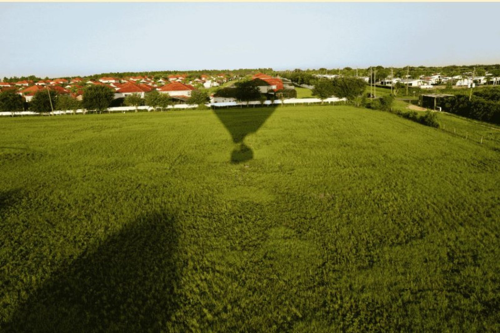Schaduw van een luchtballon valt op een groen veld tijdens een vlucht boven Lochristi