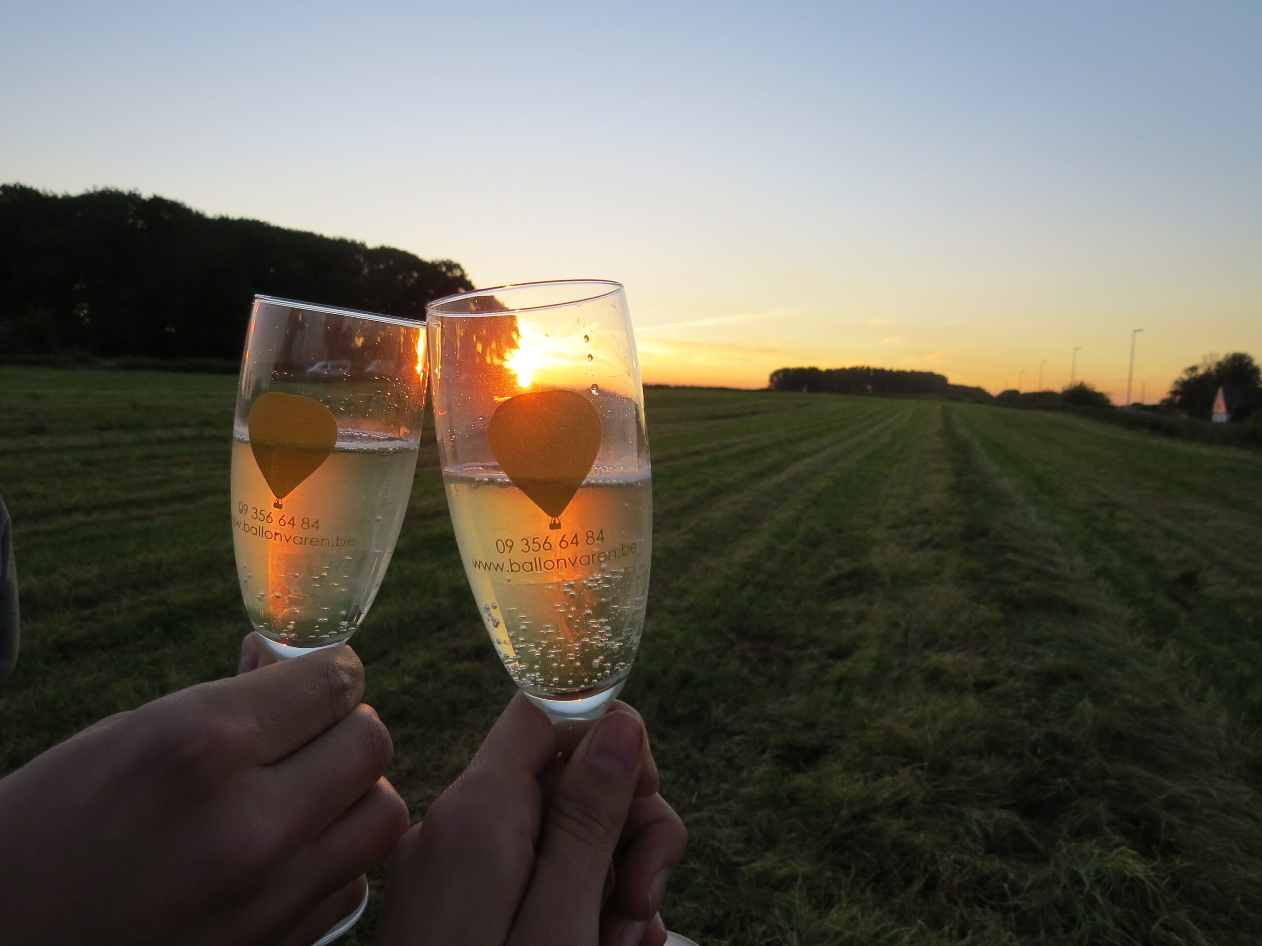 Koppel klinkt met 2 glazen champagne bij zonsondergang na een romantische ballonvaart met huwelijksaanzoek