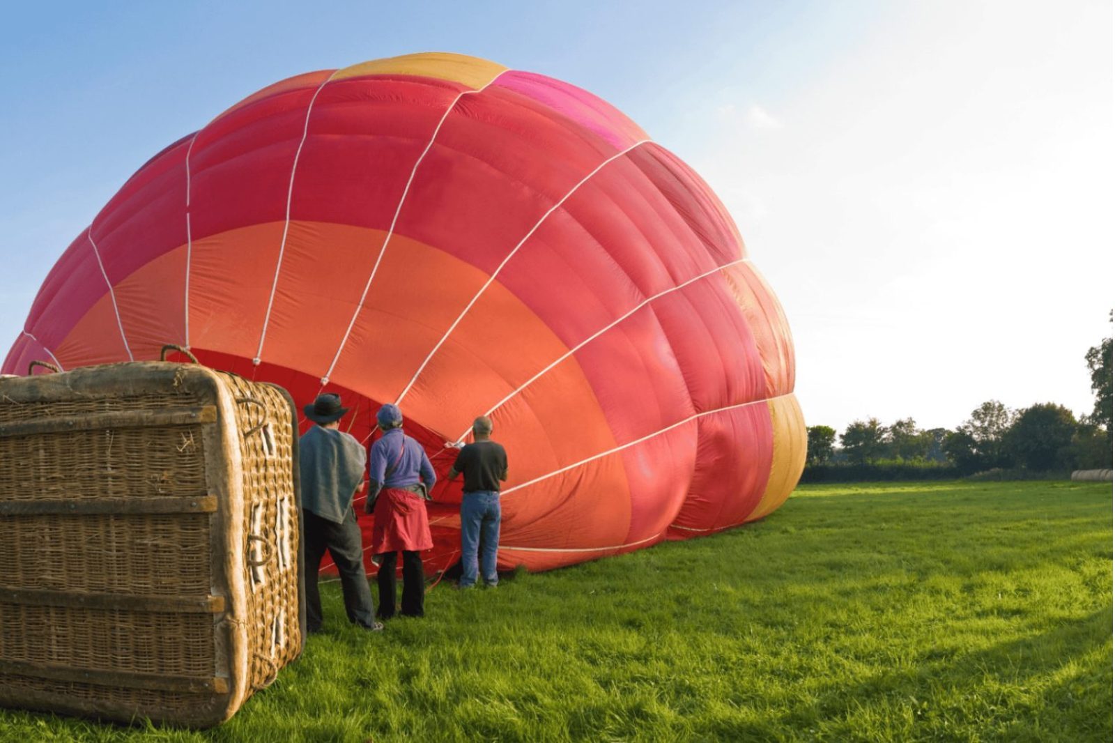 Luchtballon die wordt opgeblazen op een grasveld met crew tijdens voorbereiding van een ballonvaart