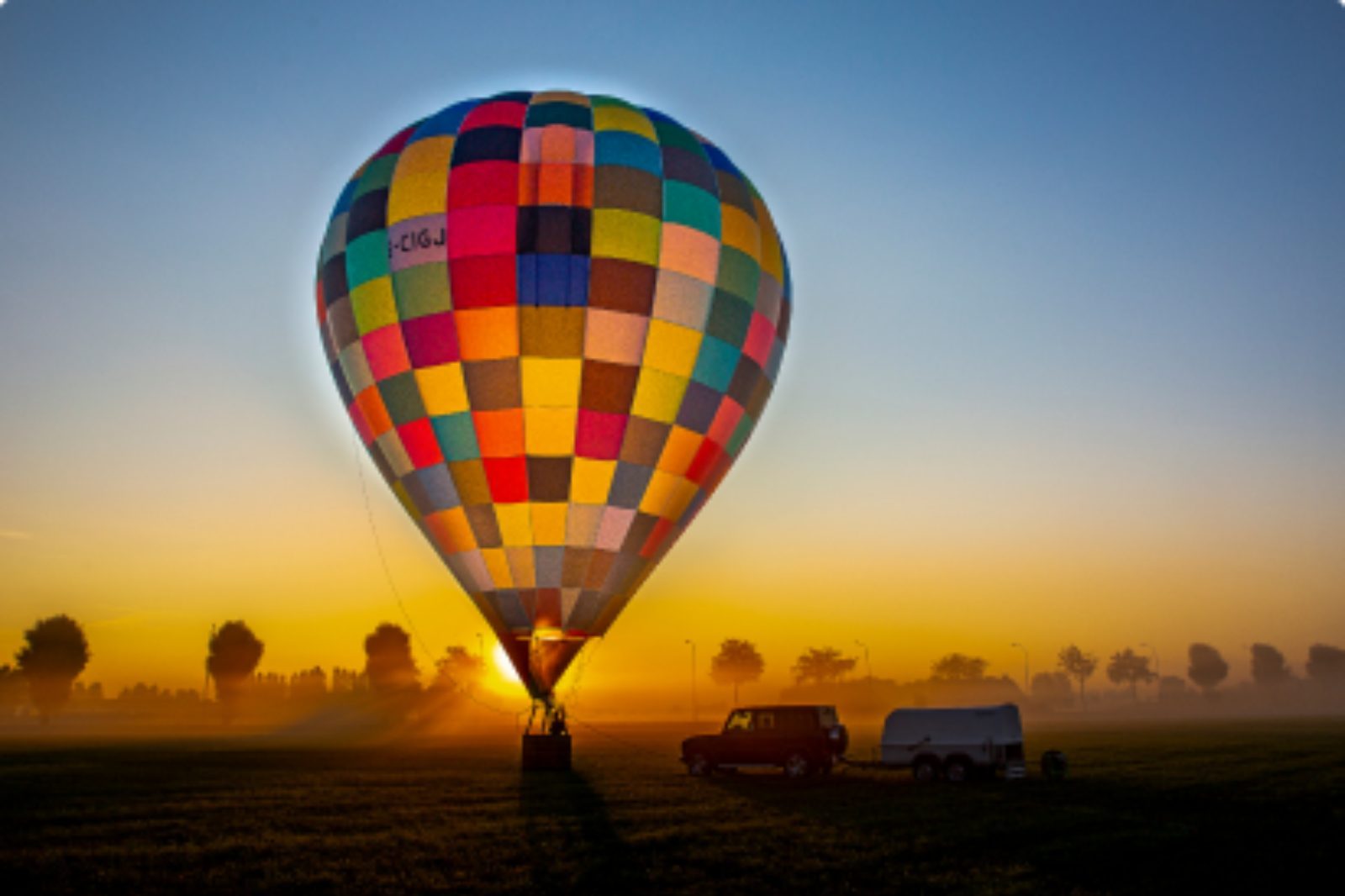 Kleurrijke luchtballon bij zonsopgang in een veld, sfeer van ballonvaart met ontbijt.