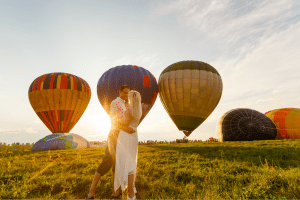 Romantisch huwelijksaanzoek tijdens een ballonvaart bij zonsondergang met een koppel tussen kleurrijke luchtballonnen op het veld.