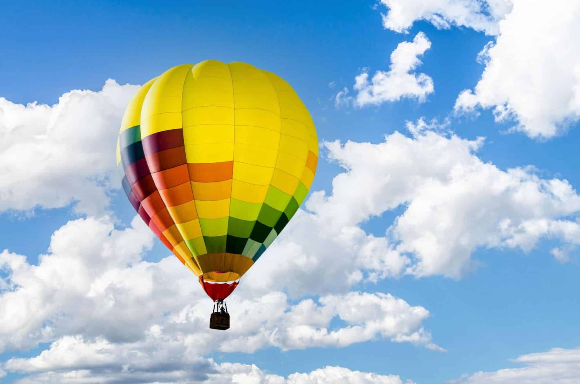 Verjaardag ballonvaart met kleurrijke luchtballon in de blauwe lucht tussen witte wolken.