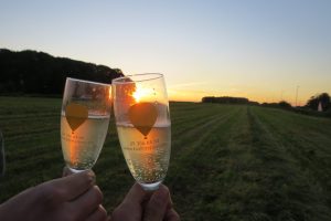 Twee glazen bubbels van ballonvaren.be klinken tegen de ondergaande zon tijdens de après-ballooning na een ballonvaart voor moederdag