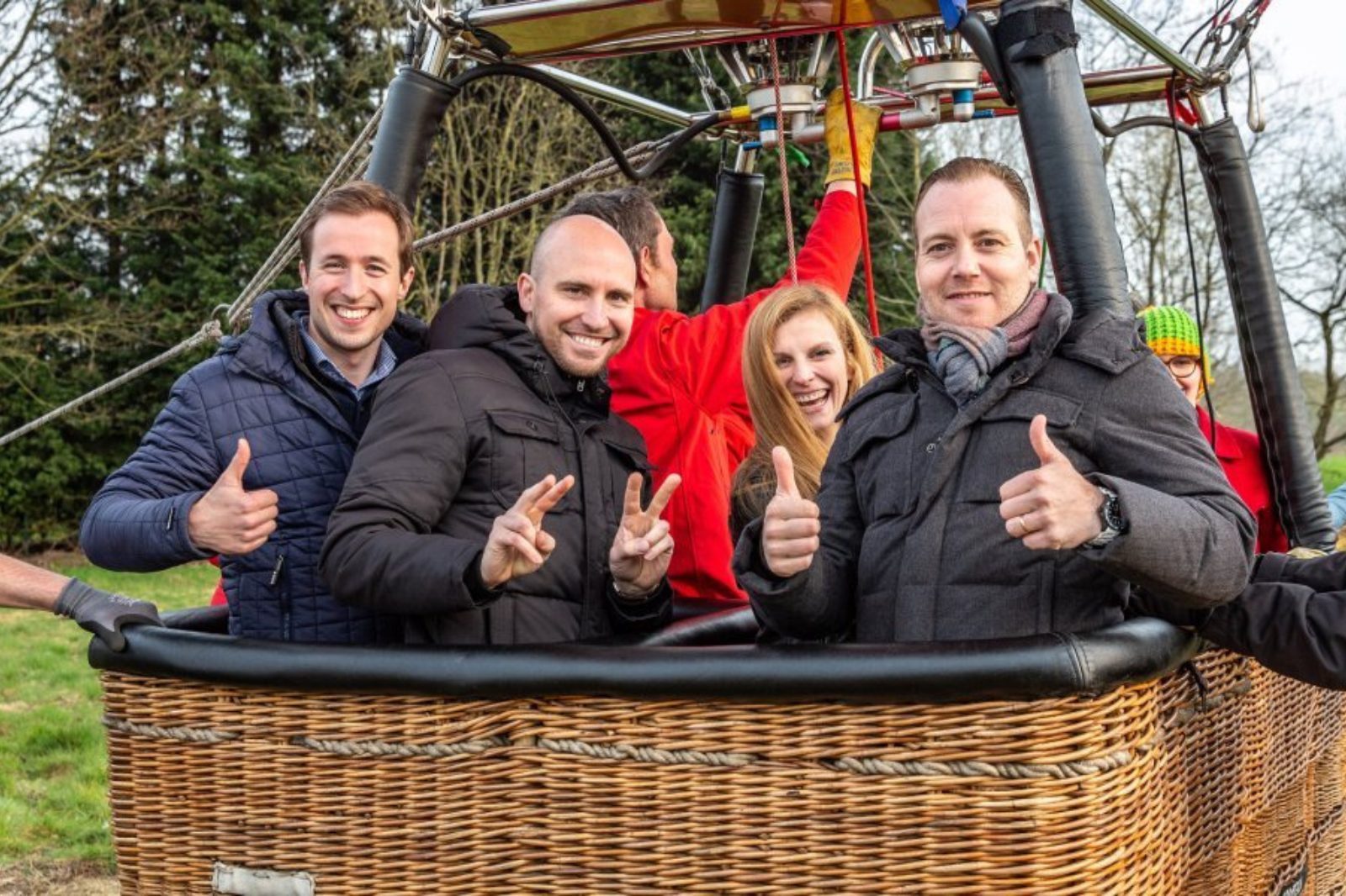 Enthousiast gezelschap poseert lachend met duimen omhoog in de ballonmand om samen een huwelijk te vieren