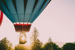 Luchtballon met koppel in de mand stijgt op tussen de bomen in het warme licht van de ondergaande zon