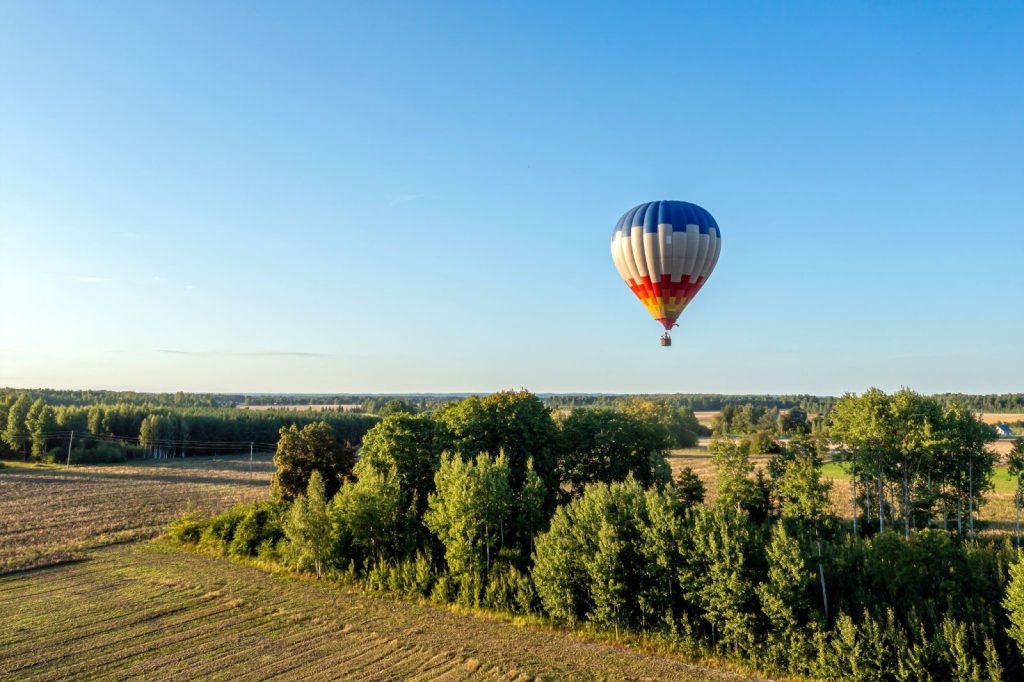 Kleurrijke luchtballon vliegt op grote hoogte boven groene velden en bossen