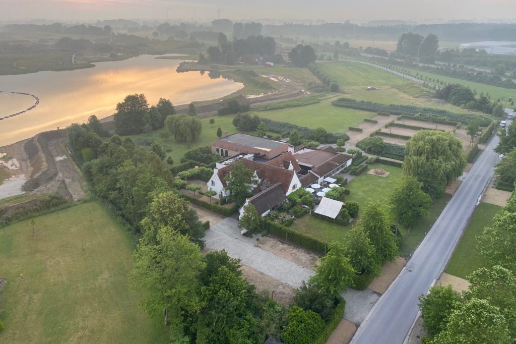 Uitzicht vanuit een luchtballon over een landgoed met vijver en velden bij zonsopgang